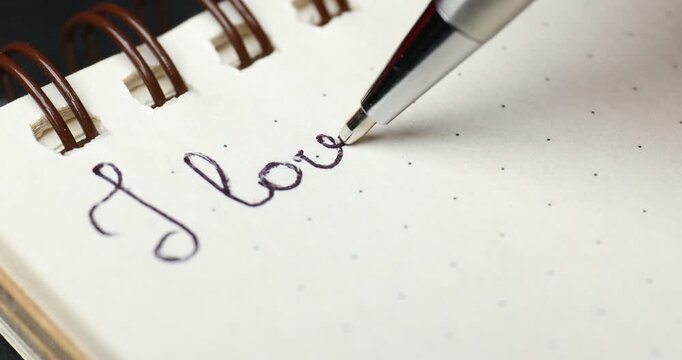 Writing phrase I Love You in notebook at table, closeup