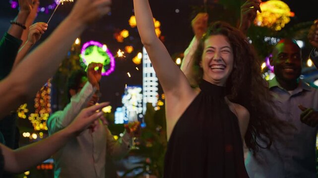 Euphoric people dance with glowing sparklers during a New Year's Eve celebration, while cheerful partygoers enjoy music and feel ecstatic as they celebrate midnight on the rooftop.