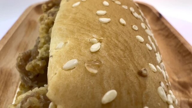 Fried chicken sub sandwich in a sesame bread roll with creamy sauce, shown from overhead and front angles on a wooden tray against a white background.