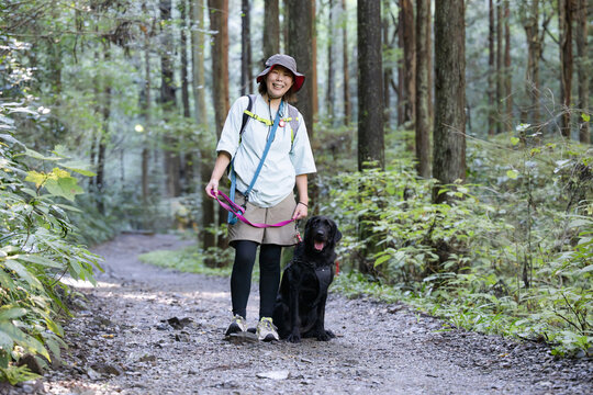 愛犬の大型犬と登山を楽しむ飼い主の全身カメラ目線、森林の中アウトドアやトレッキングのレジャーイメージ