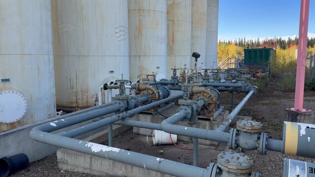 A tilt up with a slow push in on an abandoned petroleum bulk plant, showcasing rusted tanks and structures in an outdoor industrial setting.