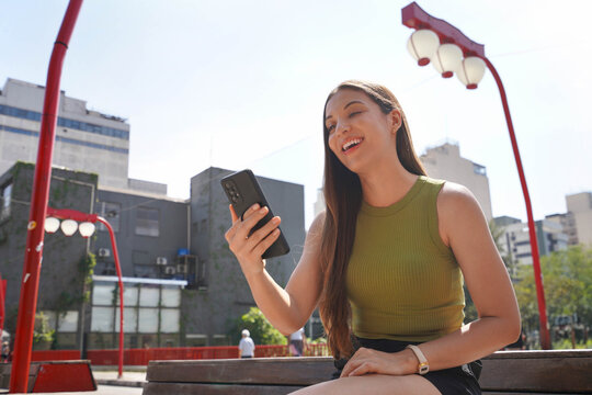 Happy tourist woman watching her smartphone sitting on bench in Liberdade neighborhood of Sao Paulo, Brazil