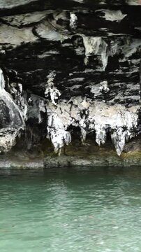 Underground limestone cave with white stalactites hanging over calm turquoise water