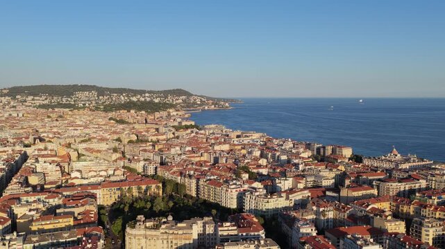 Slow sideways flight over red rooftops and a palm garden toward Baie des Anges, Castle Hill and Mont Boron, golden hour, Nice, French Riviera, Cote d Azur, France