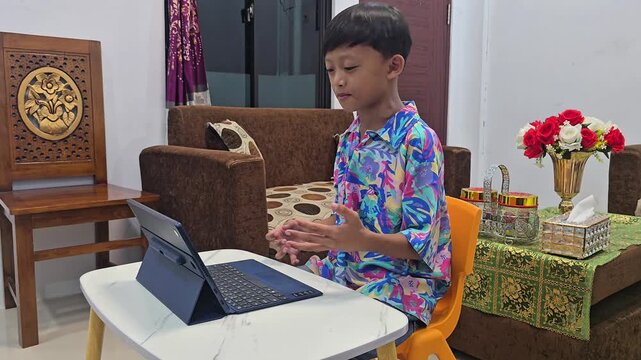 Cheerful Asian student talking and making active hand gestures during a virtual online class video call using a tablet