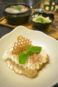 Tiramisu dessert garnished with mint leaves and honeycomb served in a white bowl