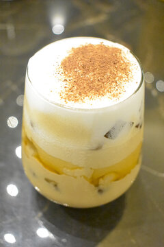 Delicious iced coffee drink with thick white milk foam and cocoa powder topping in a glass
