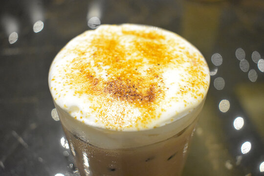 Iced coffee drink topped with rich white milk foam and sprinkled cinnamon powder