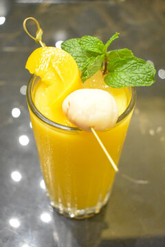 Fresh orange peach lychee juice smoothie topped with mint leaves and fresh fruits serving in a glass