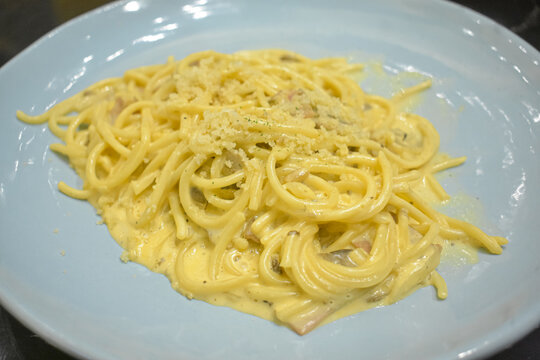 Creamy spaghetti carbonara pasta sprinkled with parmesan cheese on blue plate