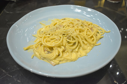 Creamy spaghetti carbonara pasta served on a light blue ceramic plate