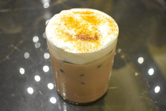 Iced coffee latte with thick white foam layer and cinnamon powder topping