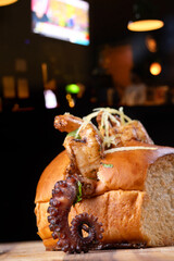 Close-up of a shrimp and octopus seafood sandwich on a wooden board, with a blurred background. © mario