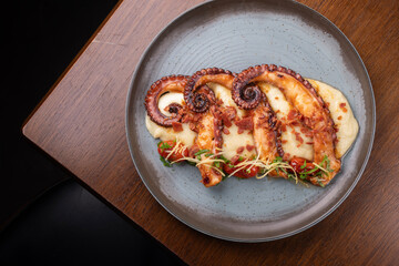 A gourmet dish featuring three tentacles of cooked octopus served with vegetable-infused mashed potatoes, set on the corner of a wooden table. © mario