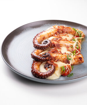 Close-up of a gourmet dish featuring three tentacles of cooked octopus served with vegetable-infused mashed potatoes against a white background.