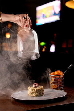 Smoking seafood tartare dish garnished with an octopus tentacle, with a blurred pub in the background.