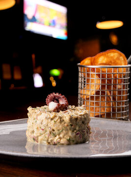 Close-up of a seafood tartare garnished with a gourmet octopus tentacle, served with potatoes at a pub.