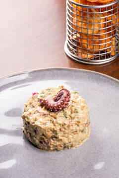 Close-up of a succulent seafood tartare garnished with a gourmet octopus tentacle, served with potatoes on a wooden table.