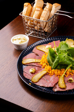 Close-up of a gourmet appetizer plate featuring pastrami, roast beef, arugula, and toast on a wooden table.