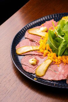 Close-up of a gourmet appetizer plate featuring pastrami, roast beef, and arugula on a wooden table.