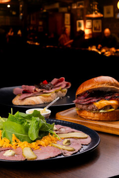 Pastrami festival featuring a cold cut platter, hamburger, and pastrami and roast beef bruschetta&mdash;restaurant menu items.