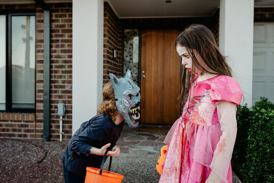 Young girl dressed as a vampire princess with her younger brother wearing a Halloween werewolf mask outside their home ready to trick or treat; Australia