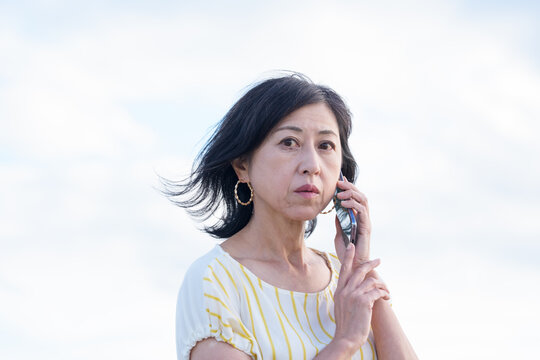 海辺で不安そうに電話を耳にあてるシニア女性