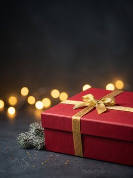Red gift box with gold glitter ribbon and bokeh lights on dark slate