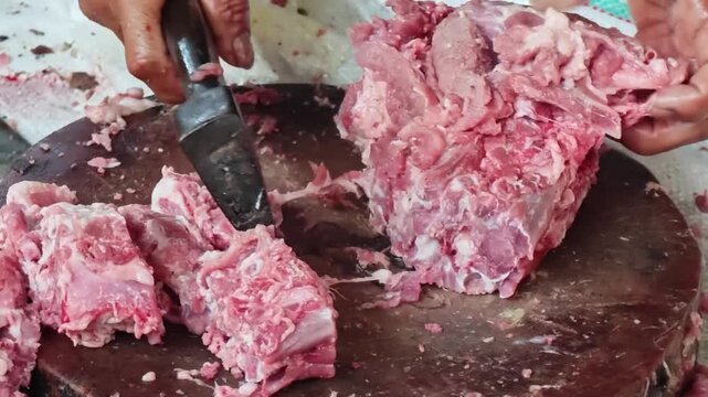 Butcher chopping raw pork ribs with a cleaver on a wooden cutting board