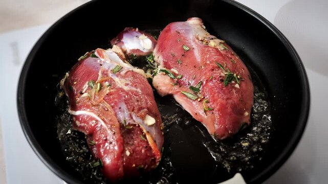 Seasoned duck breasts frying in a hot pan with rosemary and garlic. Gourmet duck meat cooks in sizzling fat during preparation of a restaurant-style meal.