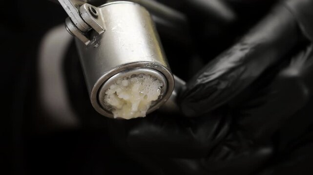 Close-up of chef crushing fresh garlic through a metal garlic press. Minced garlic comes out of the kitchen tool during cooking and ingredient preparation.
