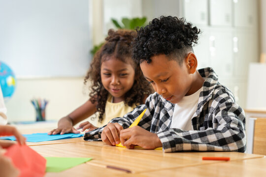 Happy school children doing origami paper craft in classroom, african american boy and girl learning arts and crafts, multi ethnic kids having fun with paper folding activity in kindergarten