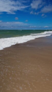 Near static vertical ground level hold as North Sea surf surges up sandy beach toward camera under bright blue sky, Scandinavia, Denmark