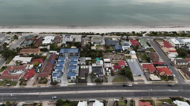 Aerial drone view along the beachfront suburb of Semaphore Park, Adelaide, South Australia, a dense mix of modern townhouses, established houses and a coastal road running parallel to beach. 