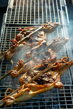 Authentic Thai grilled chicken (Kai Yang) cooking on a charcoal grill with smoky aroma. Famous Thai street food culinary culture.
