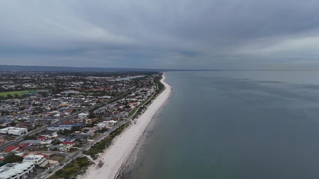 An expansive aerial drone view following the coastline of Semaphore Park in Adelaide, South Australia, with heavy cloud cover over dense waterfront residential housing.