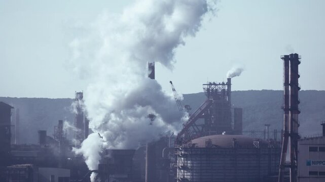 Industrial factory plant and steel mill with white smoke emitting from chimney in Muroran, Hokkaido, Japan. Cinematic heavy industry infrastructure background, fixed 4K video.