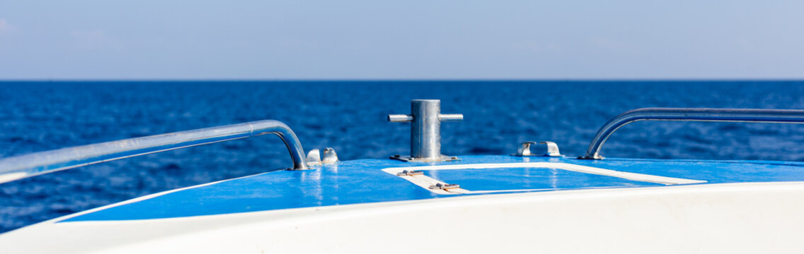 The bow of a boat sails across open blue sea water in Thailand, showing metal railings and a deck cleat.