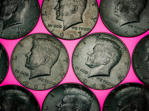 Flat lay close up of vintage US half dollar Kennedy silver coins overlapping against a bright pink background pattern