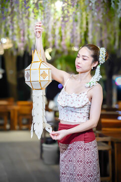 Asian woman in traditional Northern Thai dress holding a Lanna paper lantern.