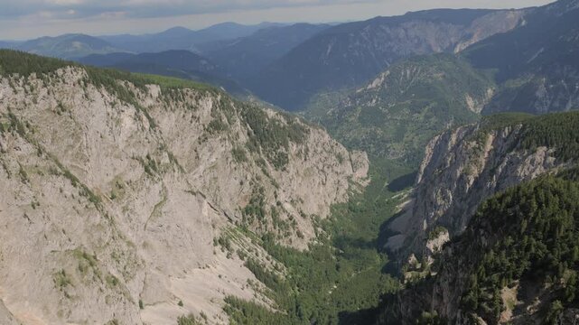Mountains rise above green valleys showing rock faces and trees in natural light.