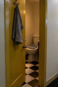 Mustard yellow painted motel bathroom door standing ajar with a folded towel on a chrome over-door hook and a folded pair of slippers