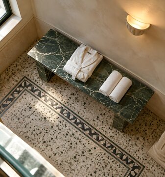 Green veined marble bench in a Roman style bathing room with a folded bathrobe and rolled towels