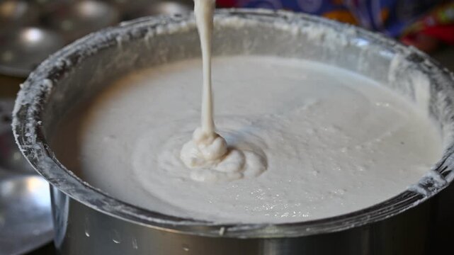 Fermented batter of idli. Smooth, airy, and freshly fermented idli batter pours into a large metal vessel. Its batter made from rice and urad dal.
