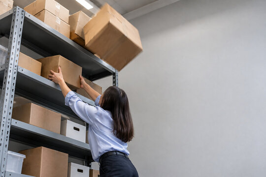 Woman Reaching Overhead Shelf as Box Falls in Office Storage Room