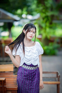 a beautiful Asian woman in traditional Thai attire posing gracefully outdoors.