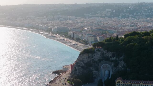 Slow tele orbit past Castle Hill cliff and war memorial toward Baie des Anges and Promenade des Anglais in hazy backlight, Nice, French Riviera, Cote d Azur, France