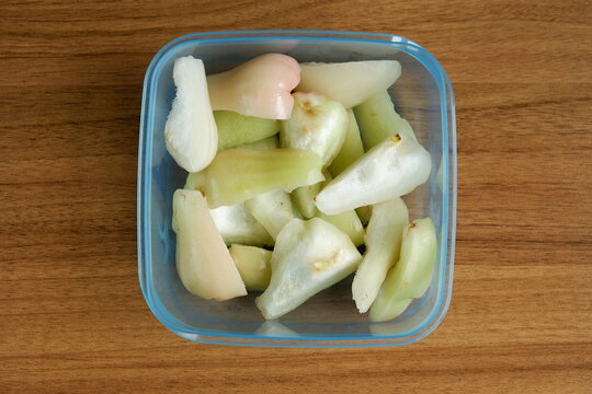 Top view of freshly cut Indonesian wax apples, known as jambu air, in a clear container on a wooden table, showcasing crisp white, green, and pink fruit pieces.