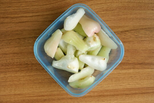 Top view of freshly cut Indonesian wax apples, known as jambu air, in a clear container on a wooden table, showcasing crisp white, green, and pink fruit pieces.