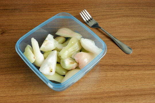 Top view of freshly cut Indonesian wax apples, known as jambu air, in a clear container and a fork on a wooden table, showcasing crisp white, green, and pink fruit pieces.